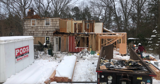 House being demolished in winter, with exposed framing, debris, and a PODS container.