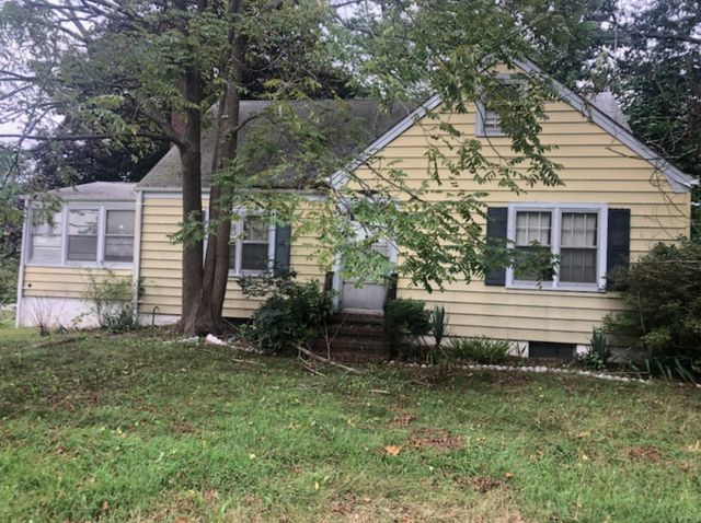 Yellow house with green shutters and overgrown lawn.