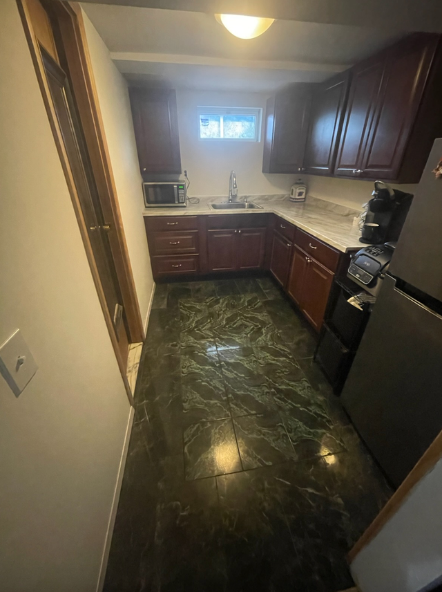 Small kitchen with dark green flooring, dark cabinets, and stainless steel appliances.