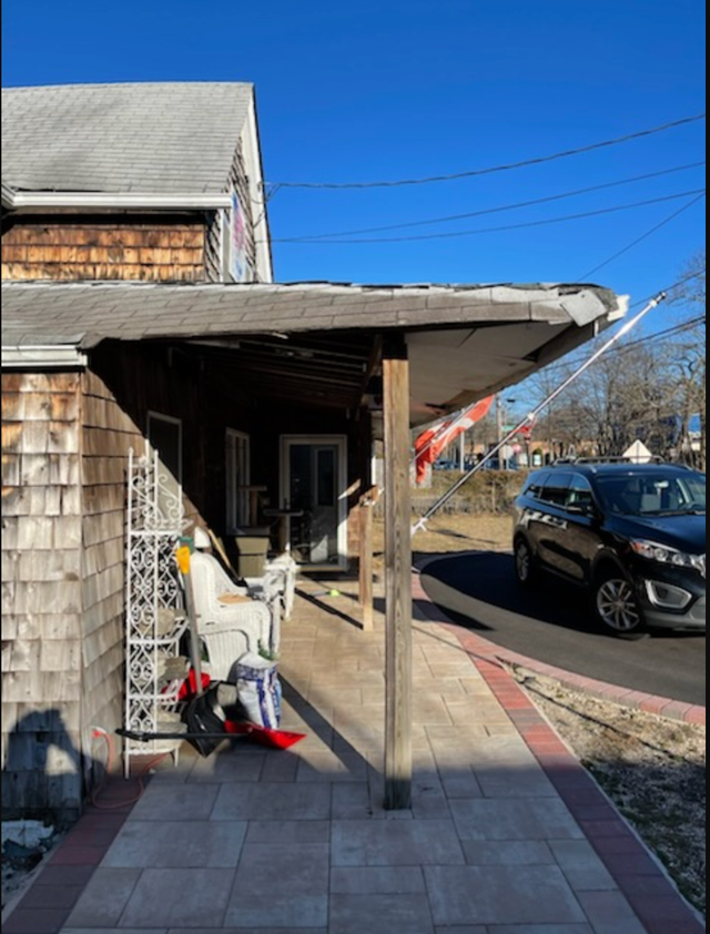 Old building with weathered wood siding and a porch, next to a sidewalk and street.