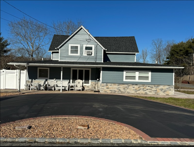Two-story blue house with a dark roof. A black driveway and lawn furniture are in front.