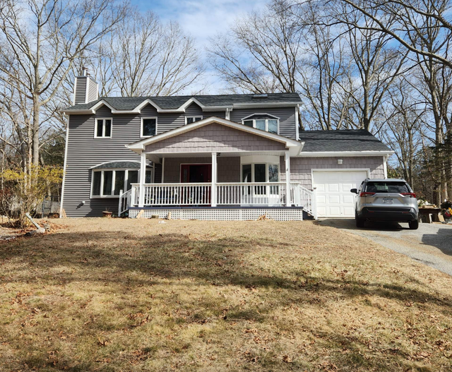 Two-story gray house with a white porch and garage, car in the driveway, trees in the background.
