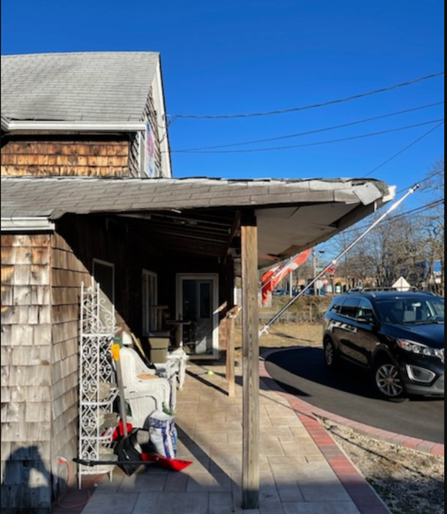 Wooden building with a porch, sidewalk, and car on the street on a sunny day.