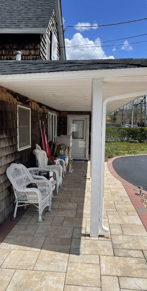 There are a lot of chairs and tables on the porch of a house.
